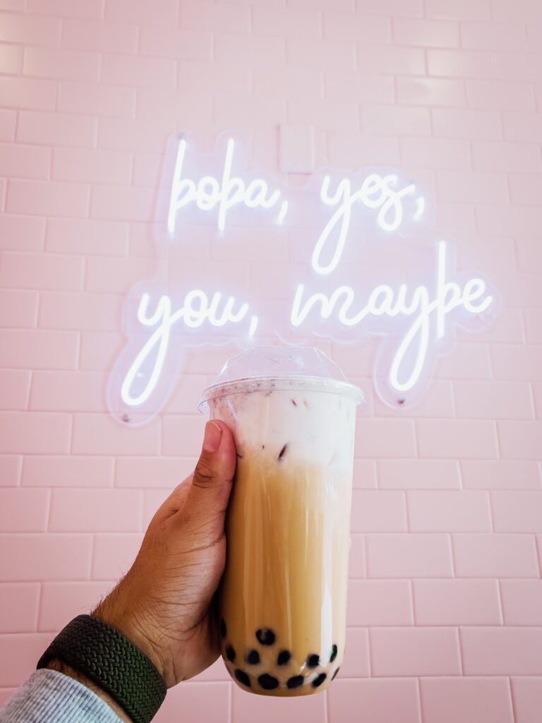 a person holding a drink in front of a neon sign